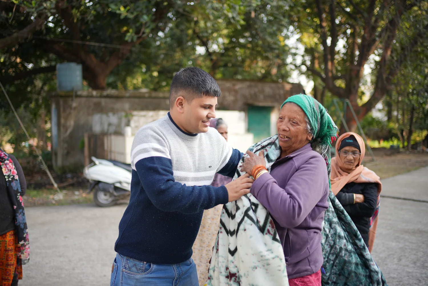 A Dev Bhoomi Samiti team member places a winter blanket around an older woman.