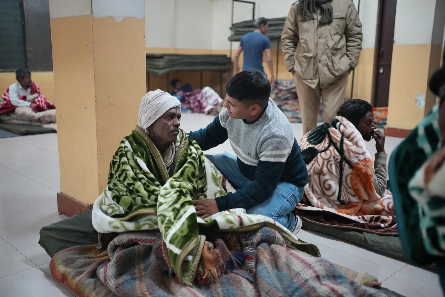 A team member helps a shelter resident put a green blanket around his shoulders.