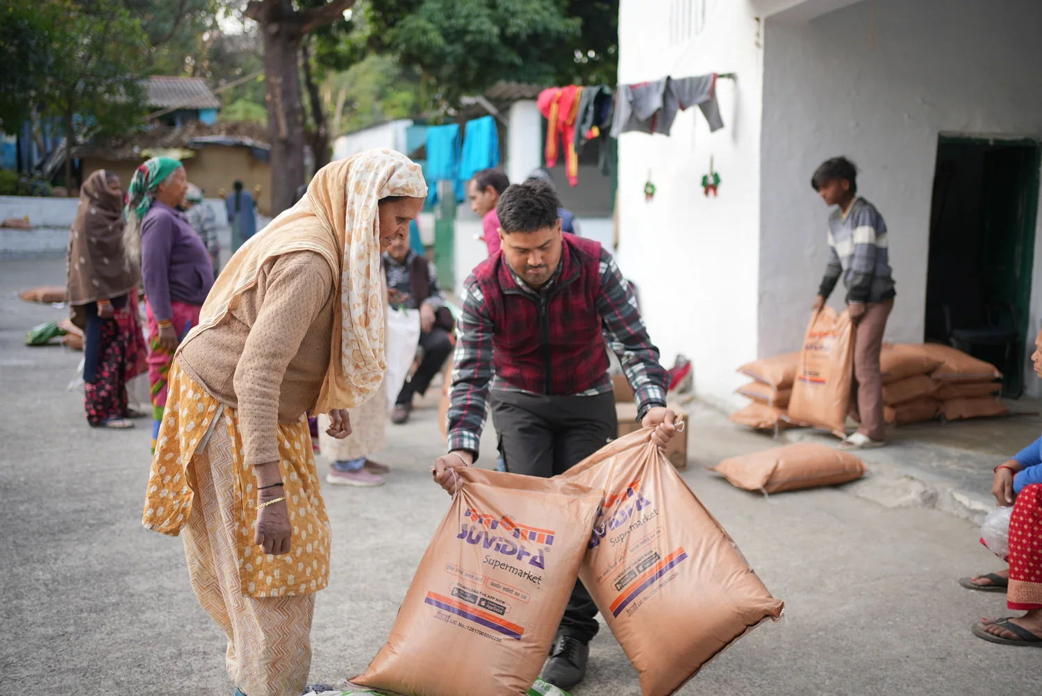 A ration bag is handed to an older woman near the community building.