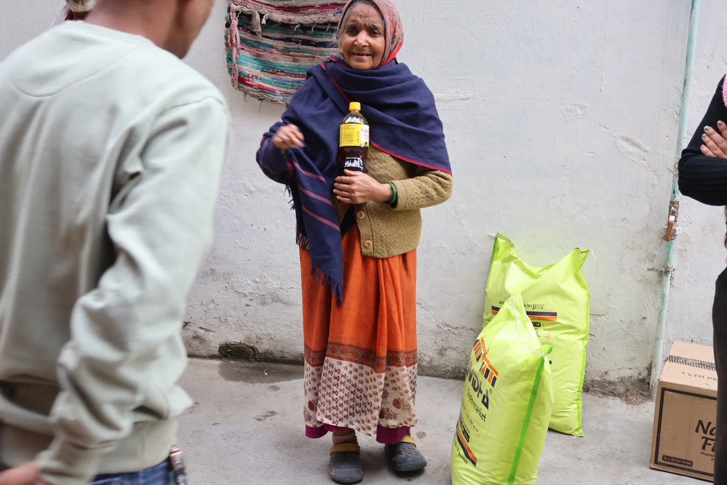 A resident holds a bottle of cooking oil beside the ration distribution area.