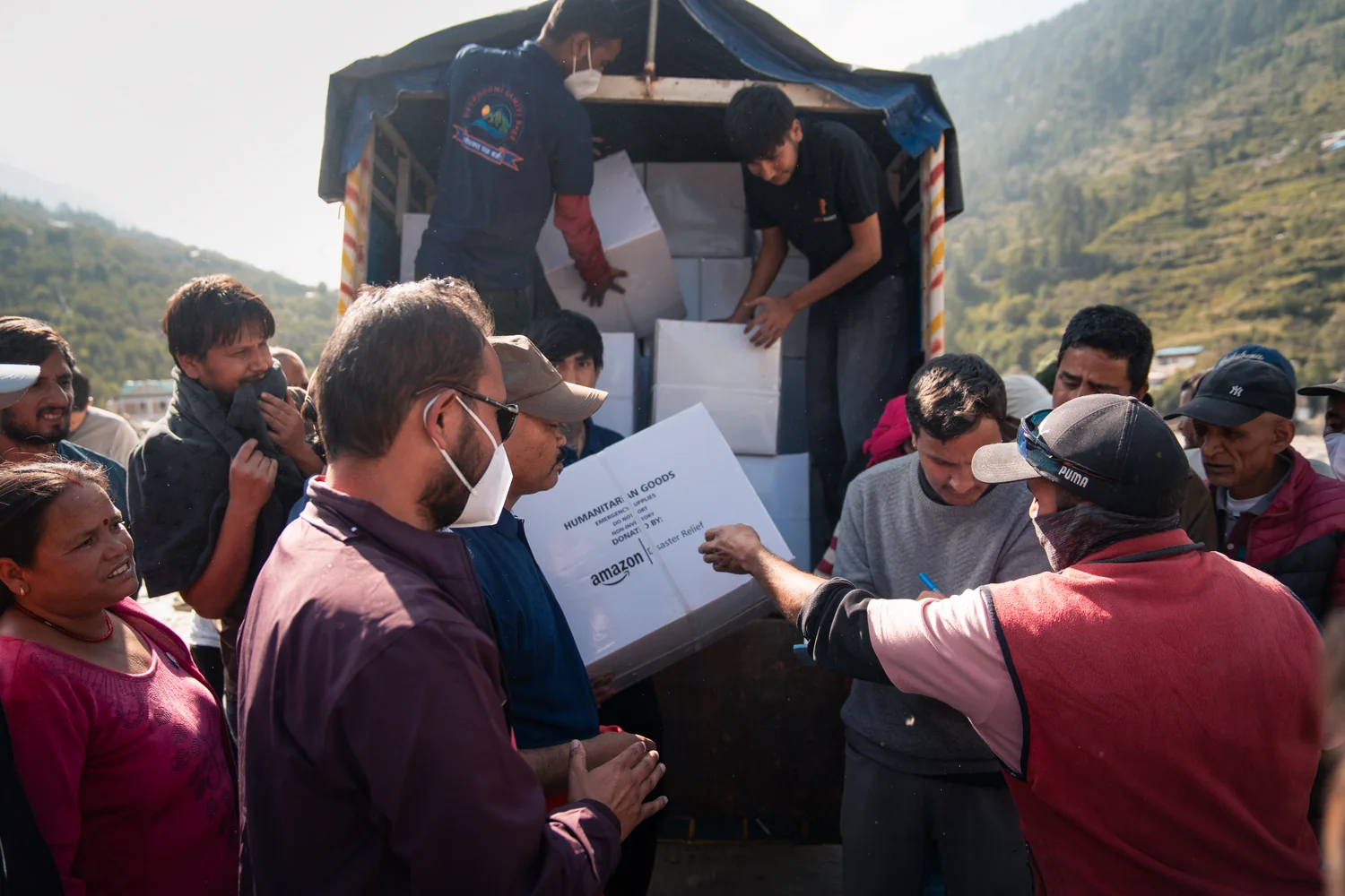 A carton of relief supplies is passed from the vehicle to people at the distribution point.