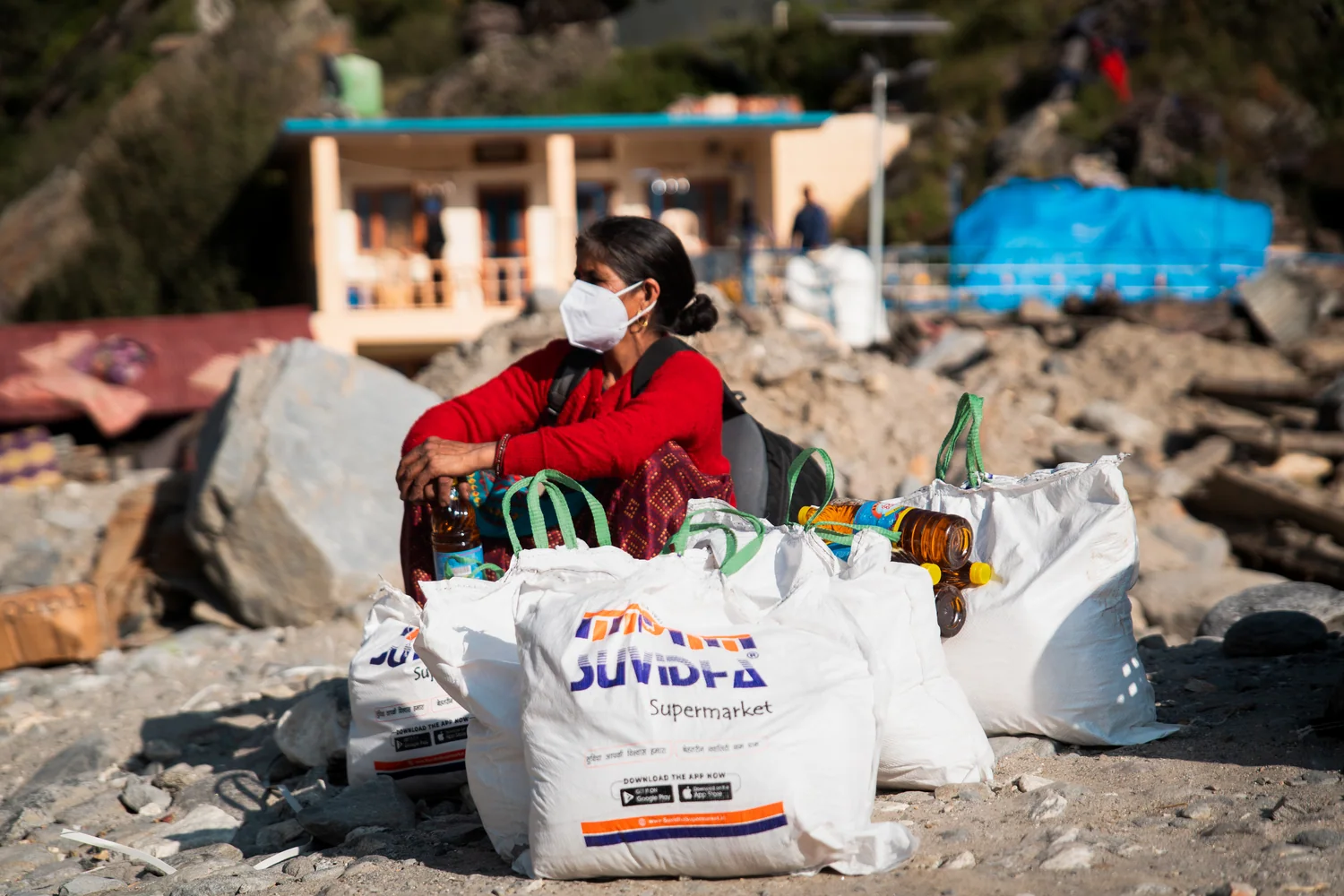 A resident sits beside collected bags and household supplies in the relief area.
