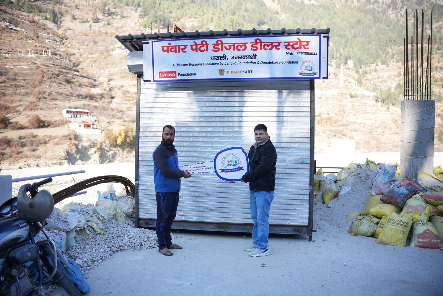 Two people stand beside a small shop structure in the Dharali recovery archive.
