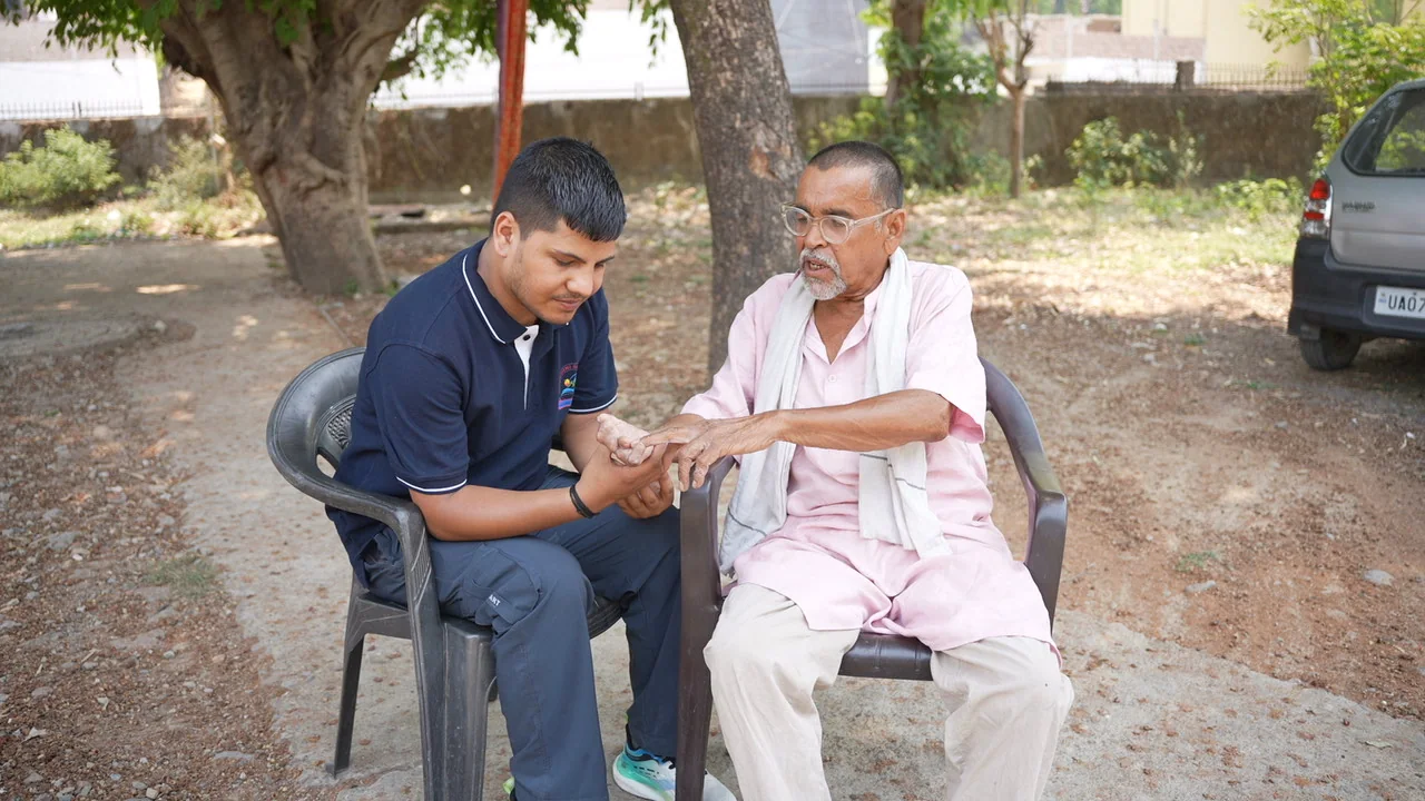 A team member sits beside an older man during a community visit.