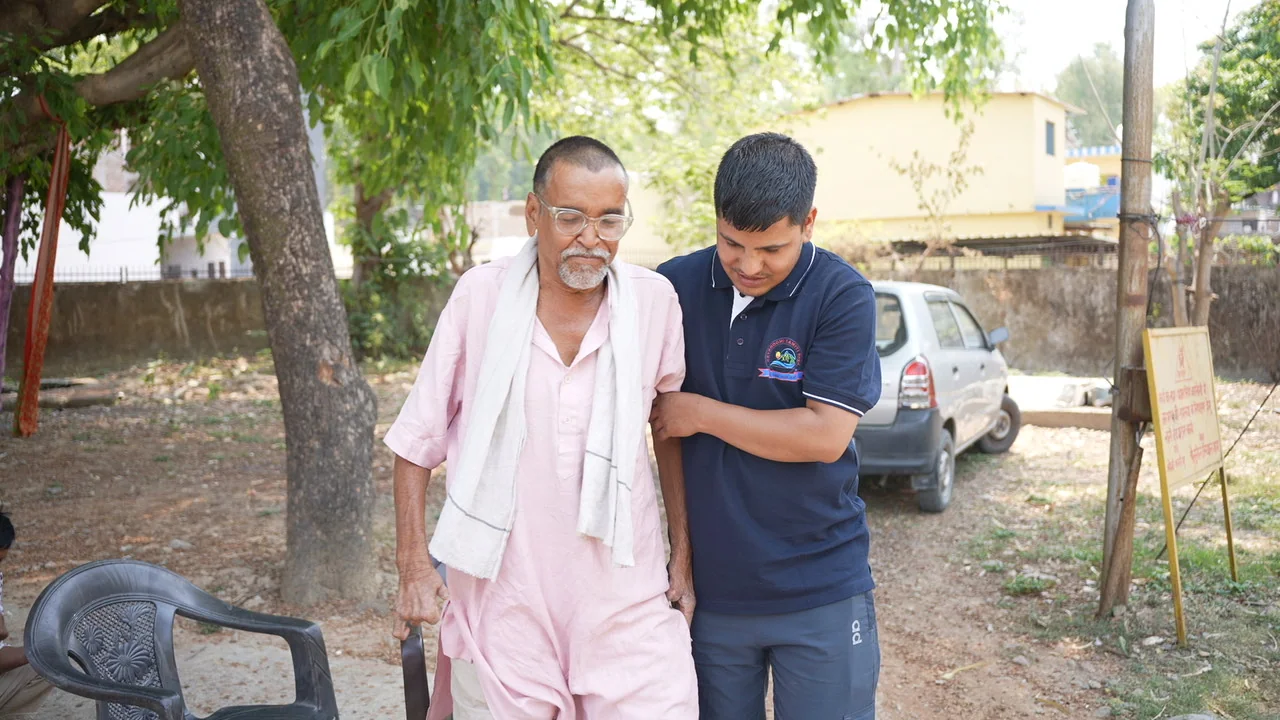 An older resident is offered support while walking outdoors.