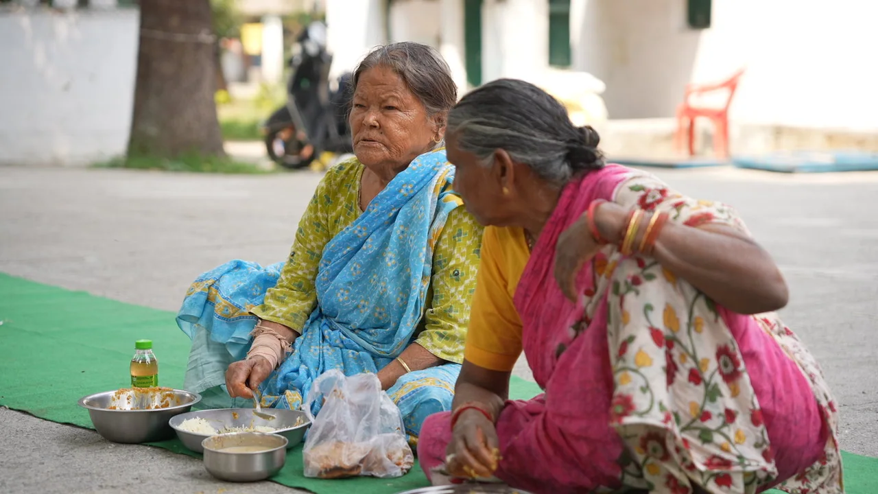 Older women sit together with their meals at the community gathering.