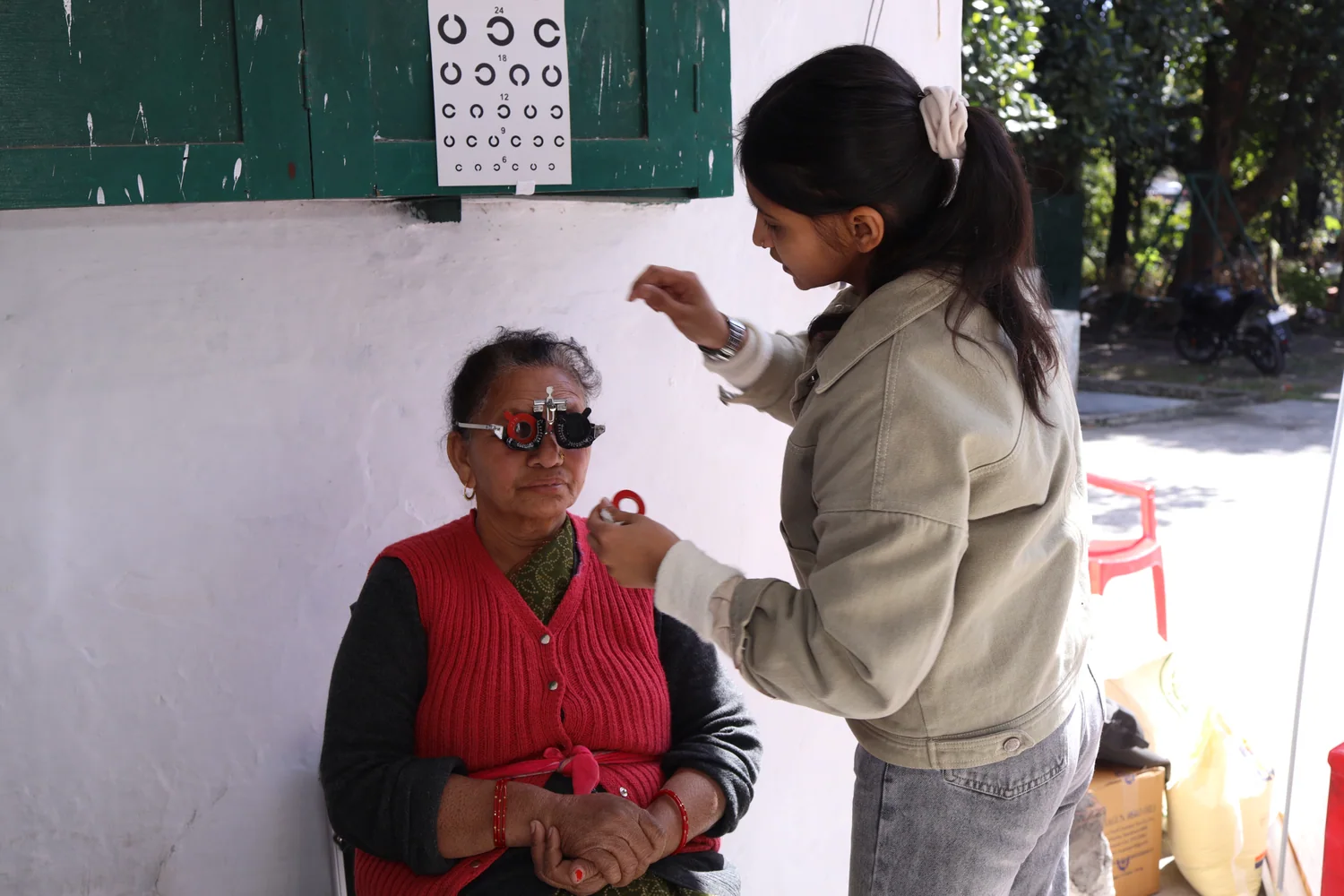 A resident uses trial lenses while the eye-care team indicates the vision chart.