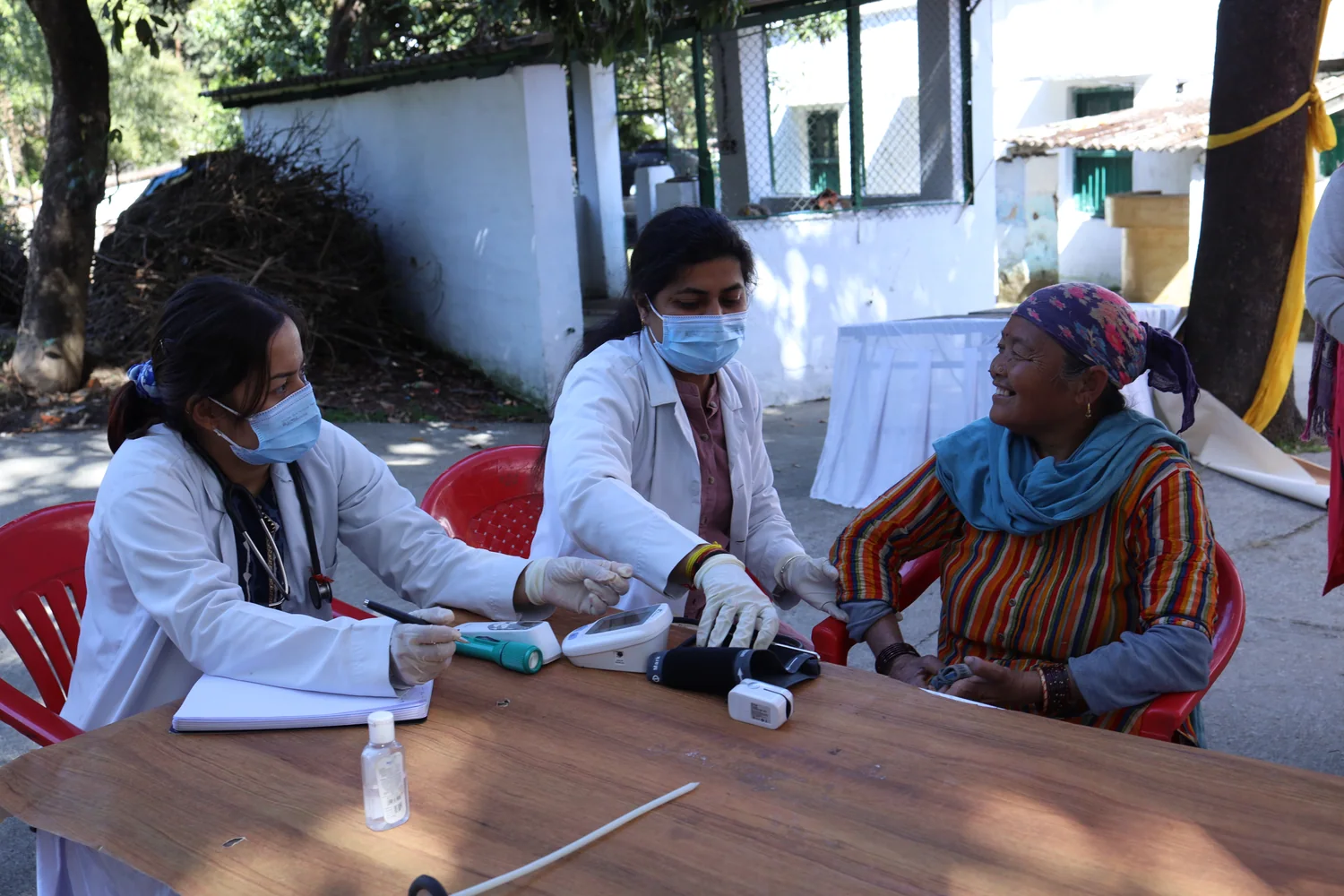 The health team speaks with a resident at an outdoor consultation table.