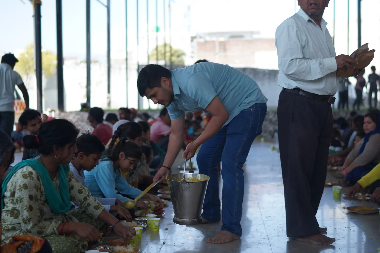 A volunteer serves food to children seated in the meal area.