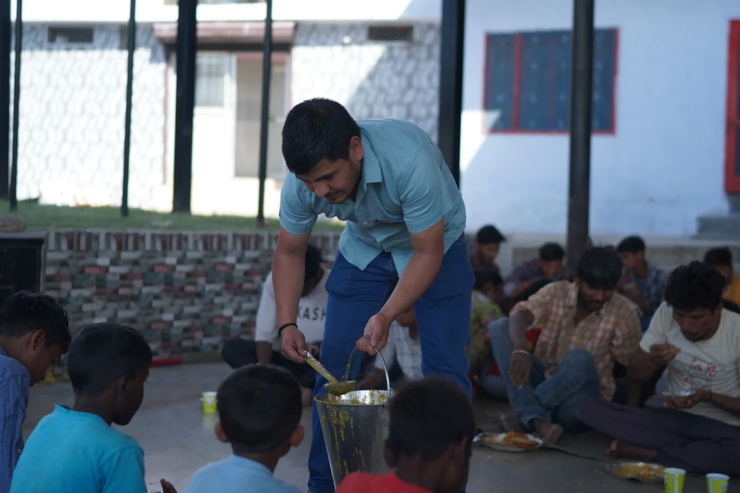 A volunteer serves food from a container to people seated for the meal.