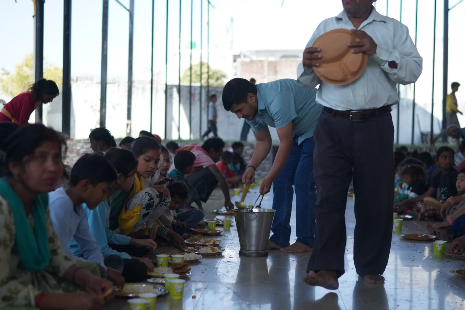 A serving volunteer carries food between the rows of seated guests.