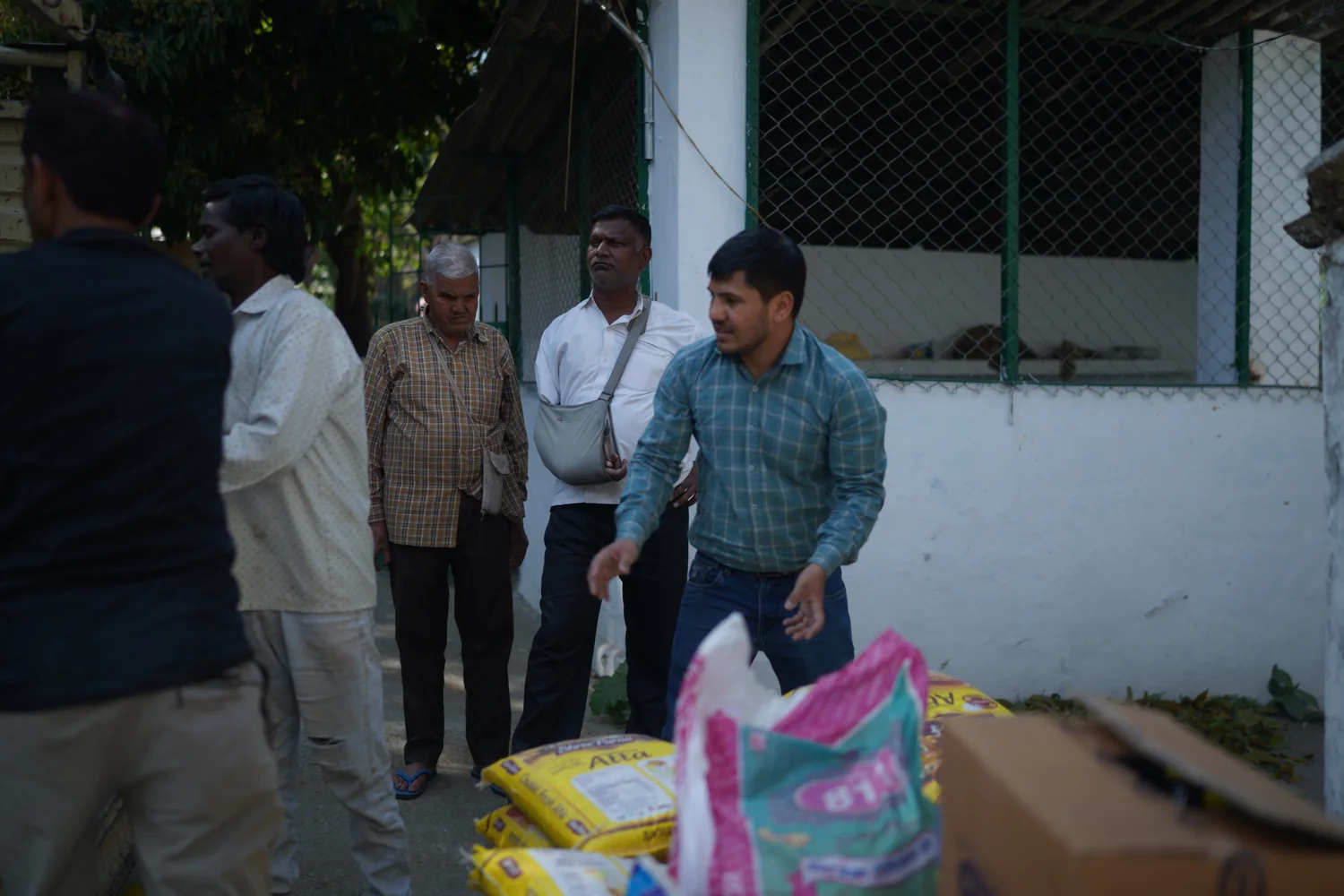 Team members stand beside ration bags near the building.