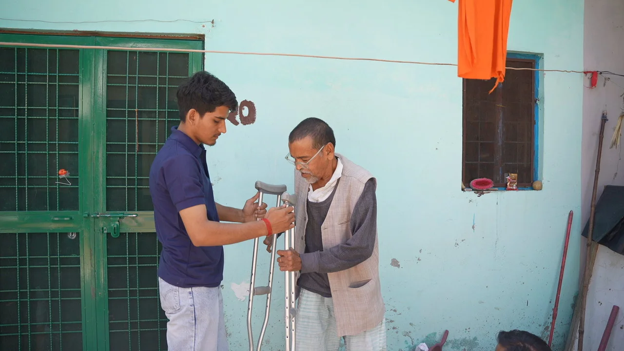 A team member stands beside an older resident using crutches.