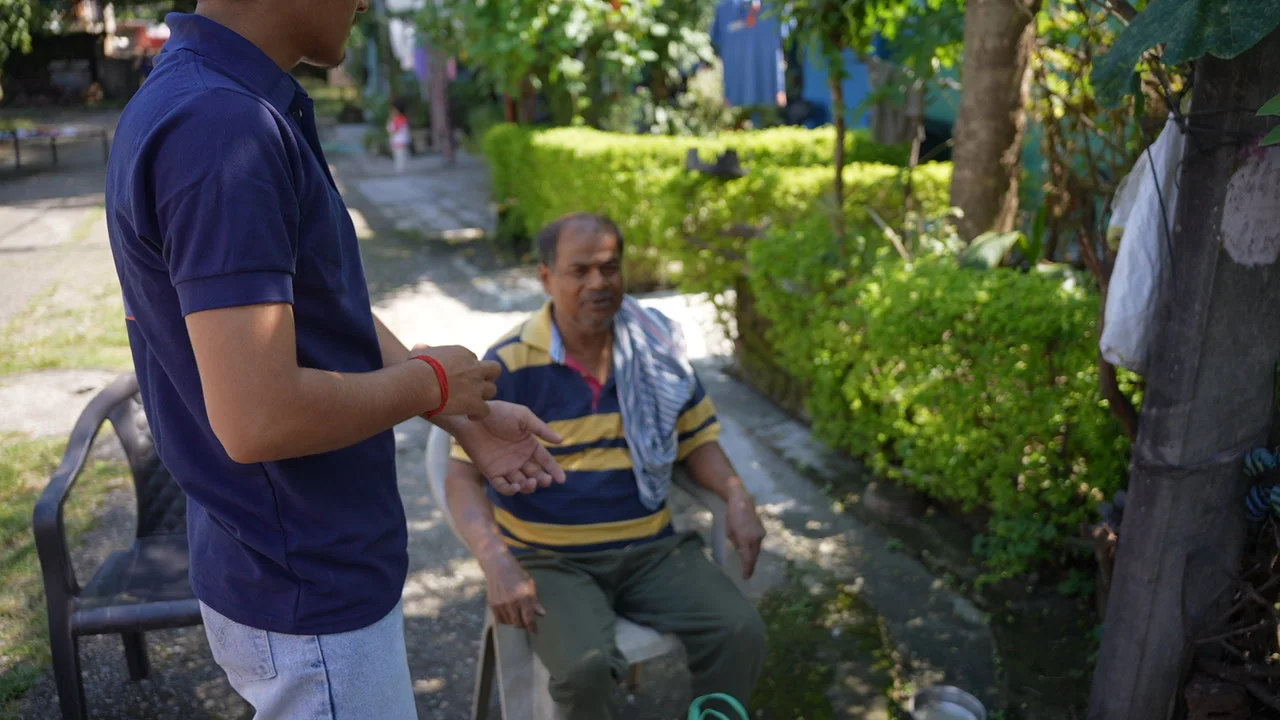 A visitor speaks with an older man seated in the courtyard.