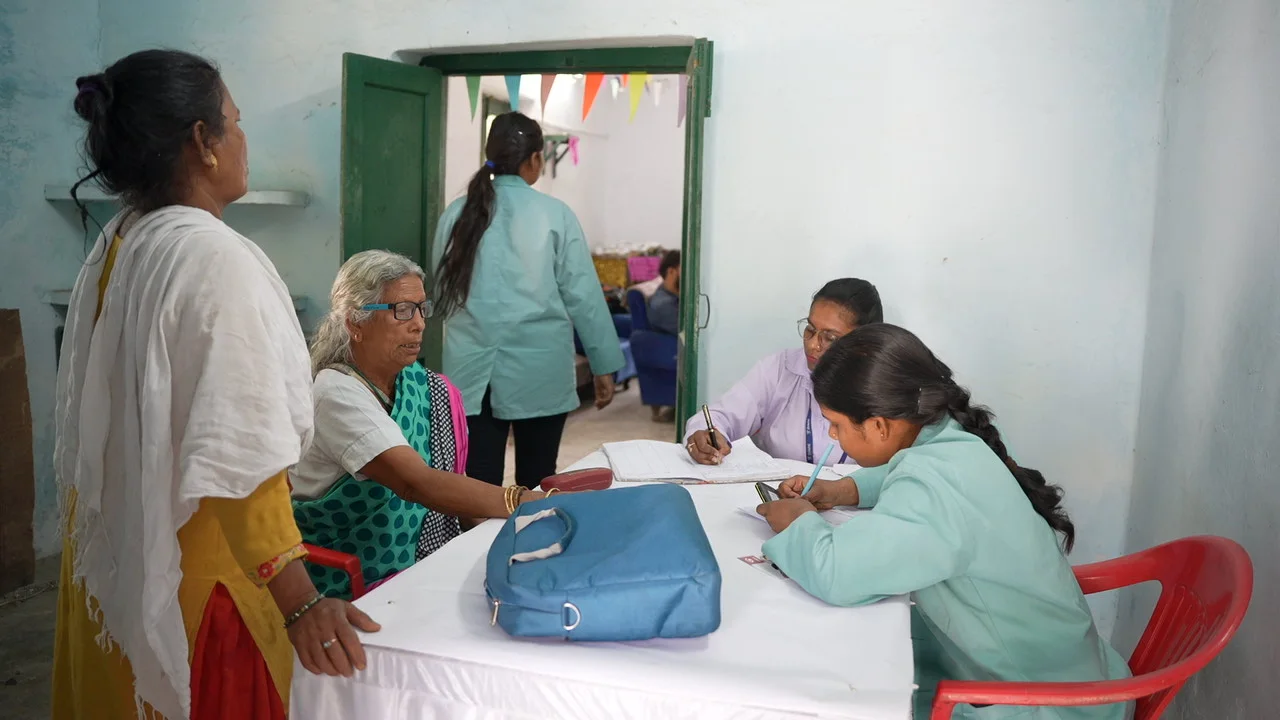 Residents and health workers speak at tables inside the session room.