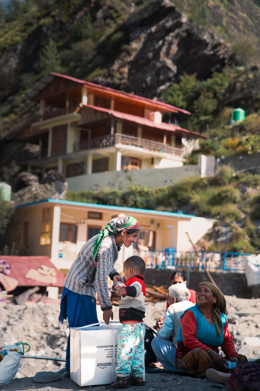 Residents stand beside collected supplies in the Dharali relief area.