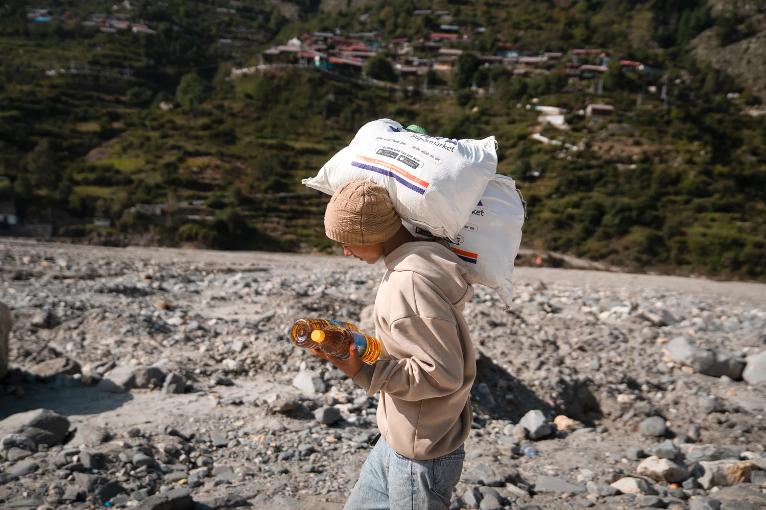 A resident carries a sack through uneven ground near Dharali.