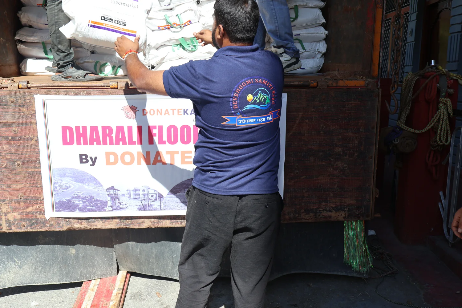 A team member helps arrange the load beside the Dharali relief banner.