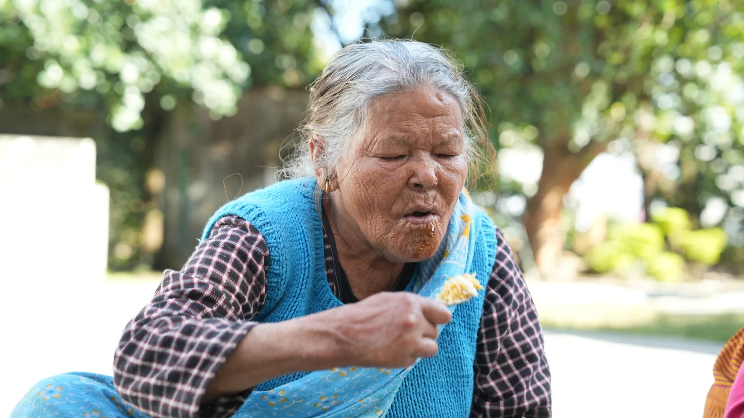 An older woman eats during the outdoor outreach gathering.