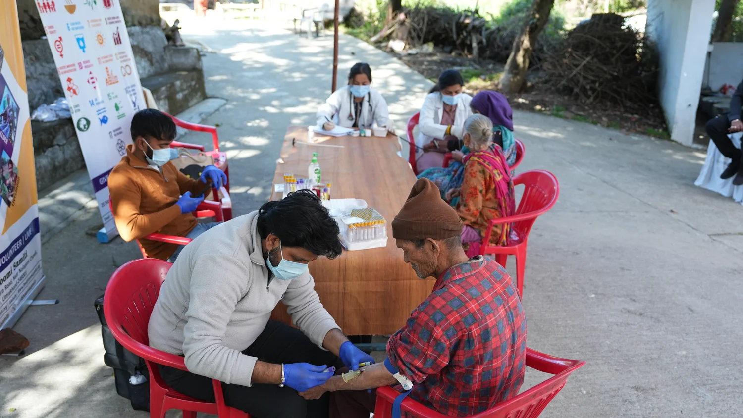 Health workers and residents meet at outdoor consultation tables.