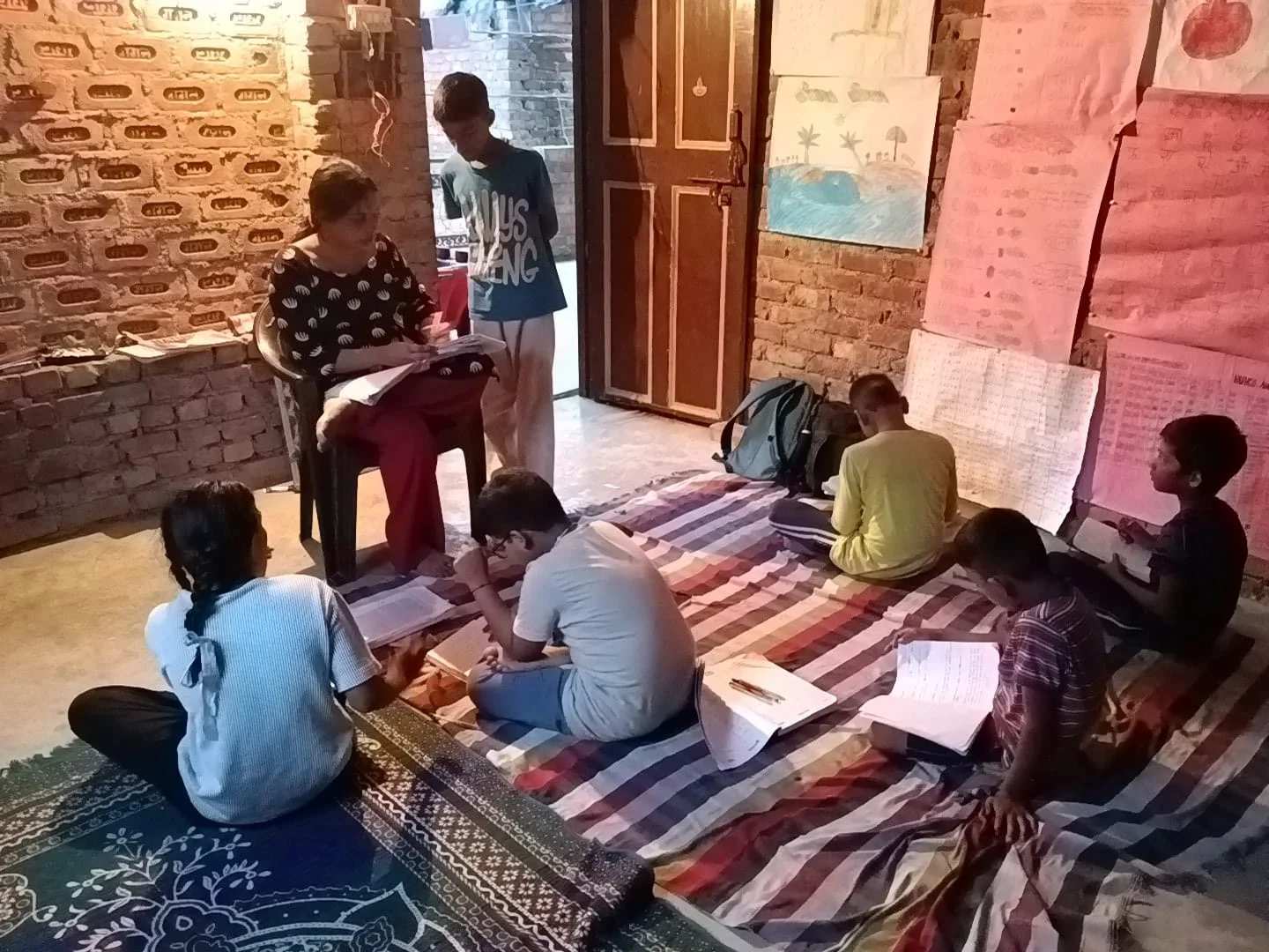 A teacher works with children and their notebooks in the community learning room.