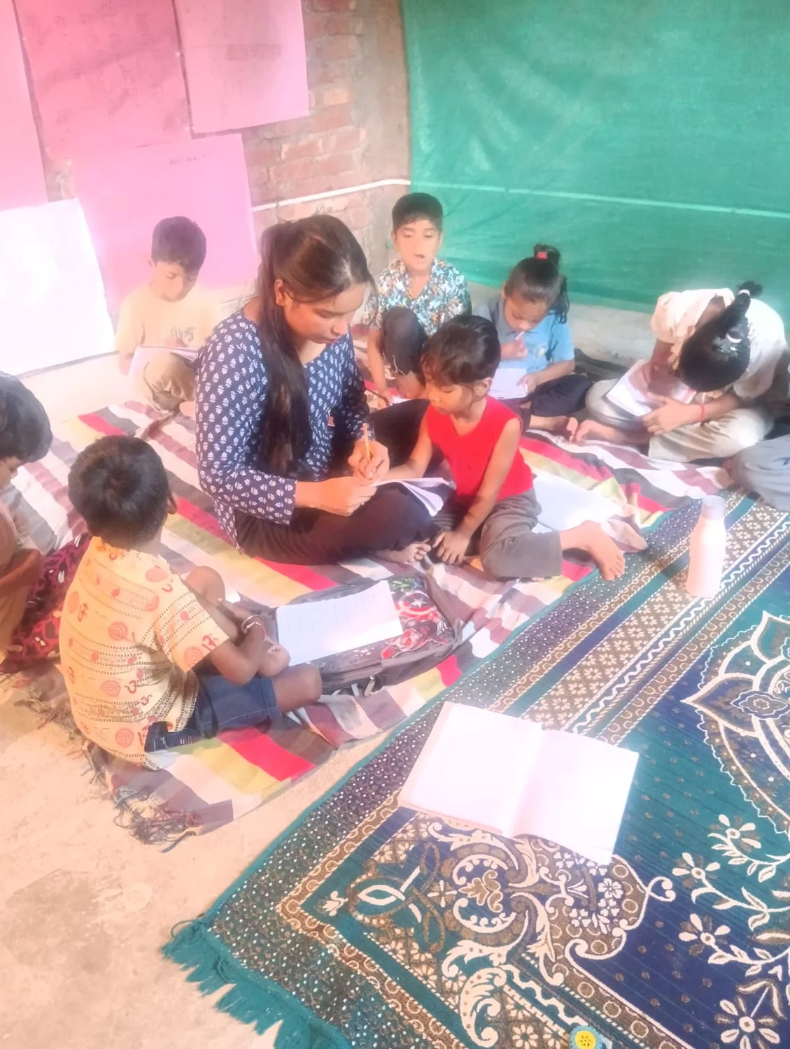 A teacher looks at a child’s notebook while other learners work nearby.
