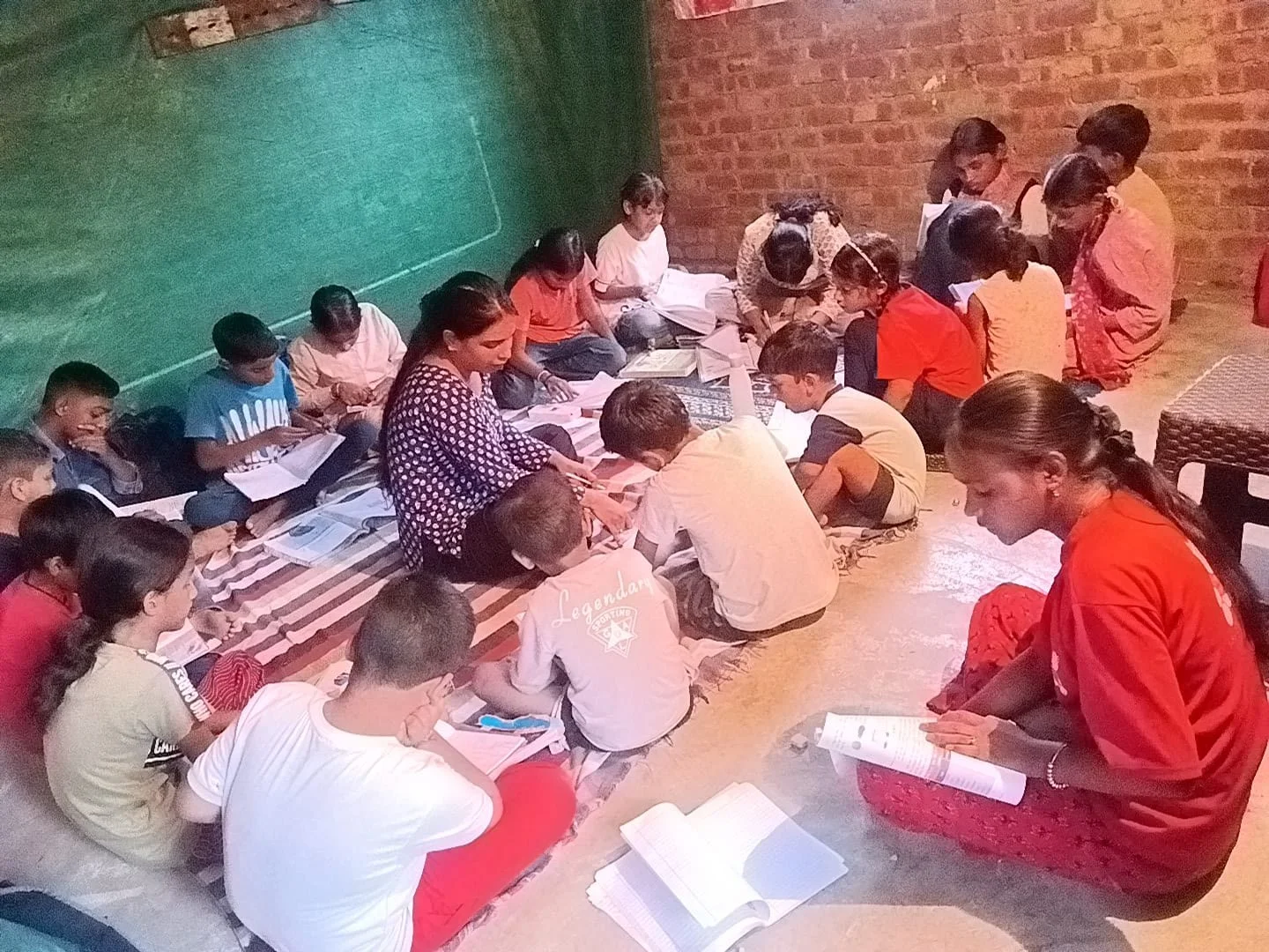 A teacher sits among children to support notebook work during the session.