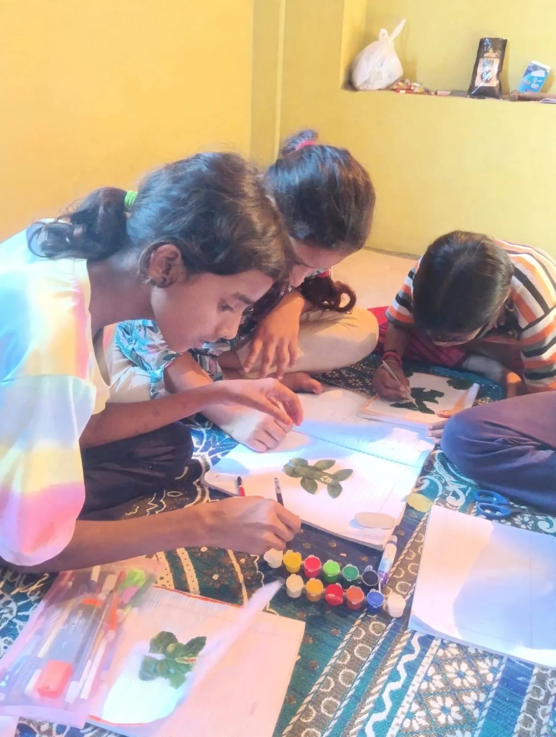 Children work together with leaves, paper and small paint pots.