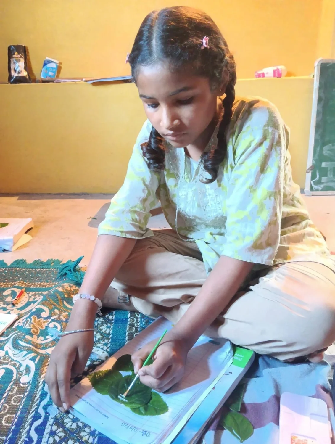 A learner carefully paints a leaf-based artwork in her notebook.