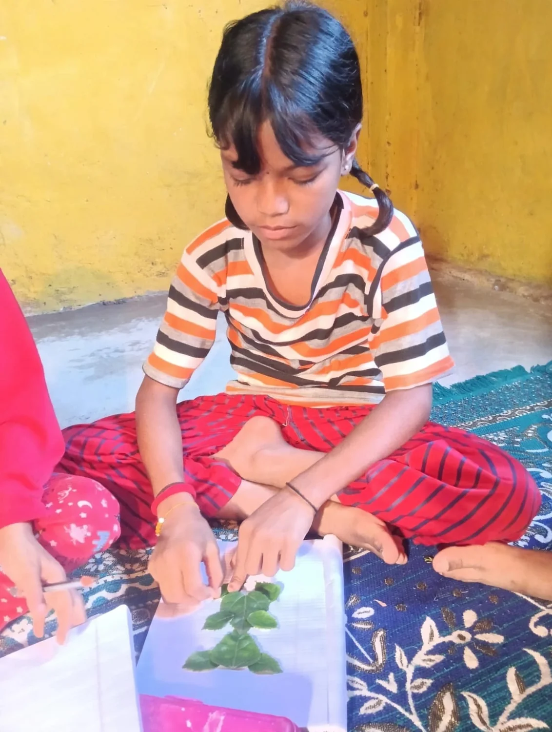 A child arranges leaves on paper during the creative activity.