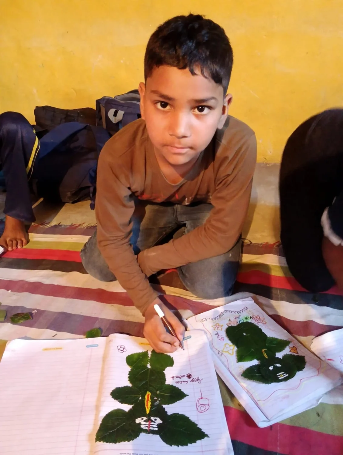 A child uses a fine brush to decorate a leaf-based Ganesh artwork.