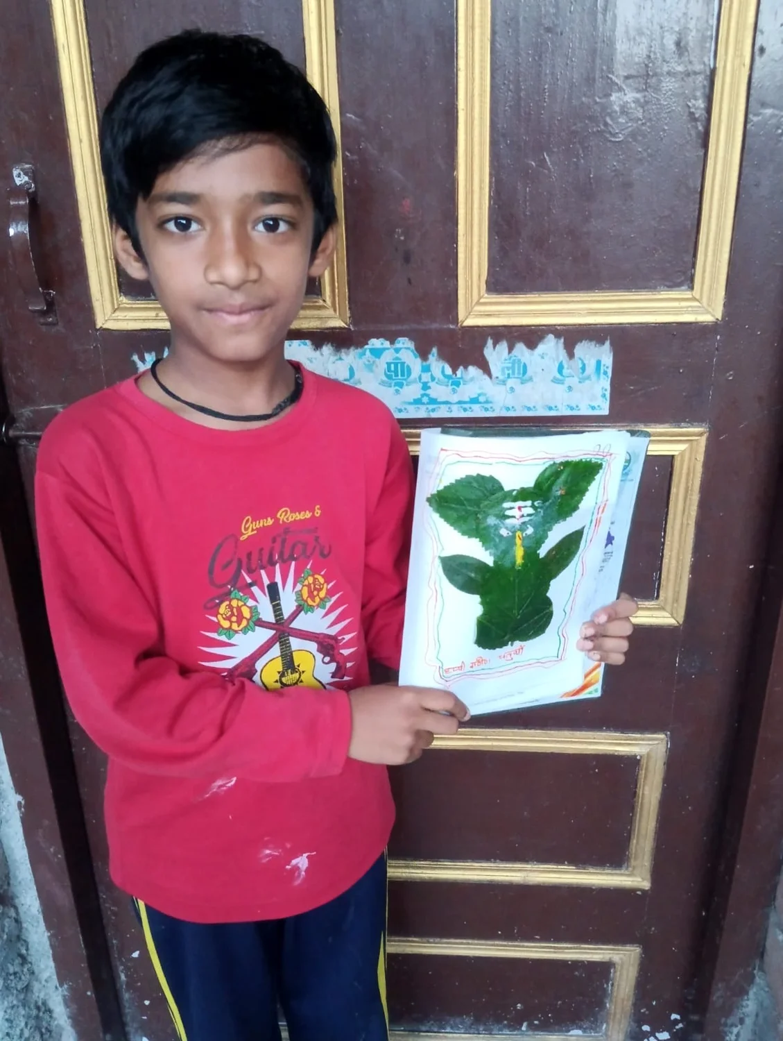 A learner holds up a finished artwork made with leaves and painted details.