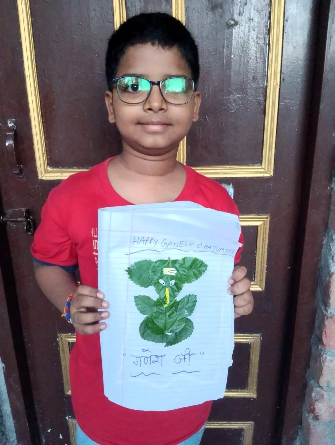 A child presents a completed Ganesh-themed leaf artwork on a notebook page.
