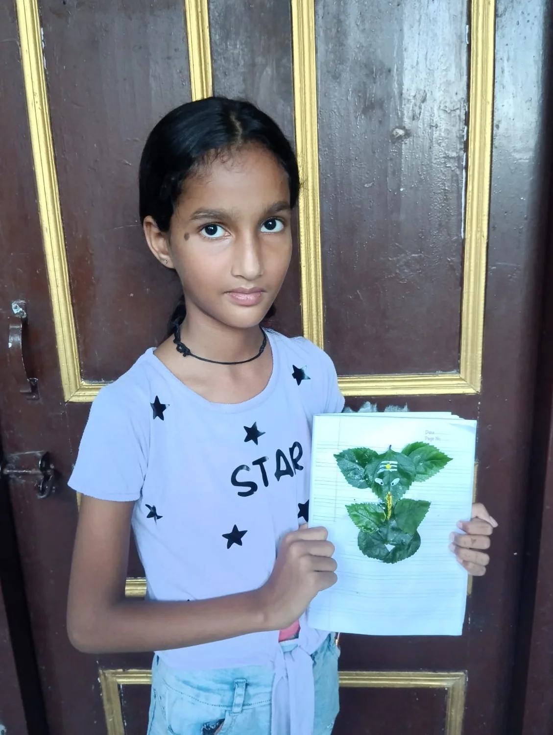 A learner shows her finished leaf artwork beside the learning room doorway.