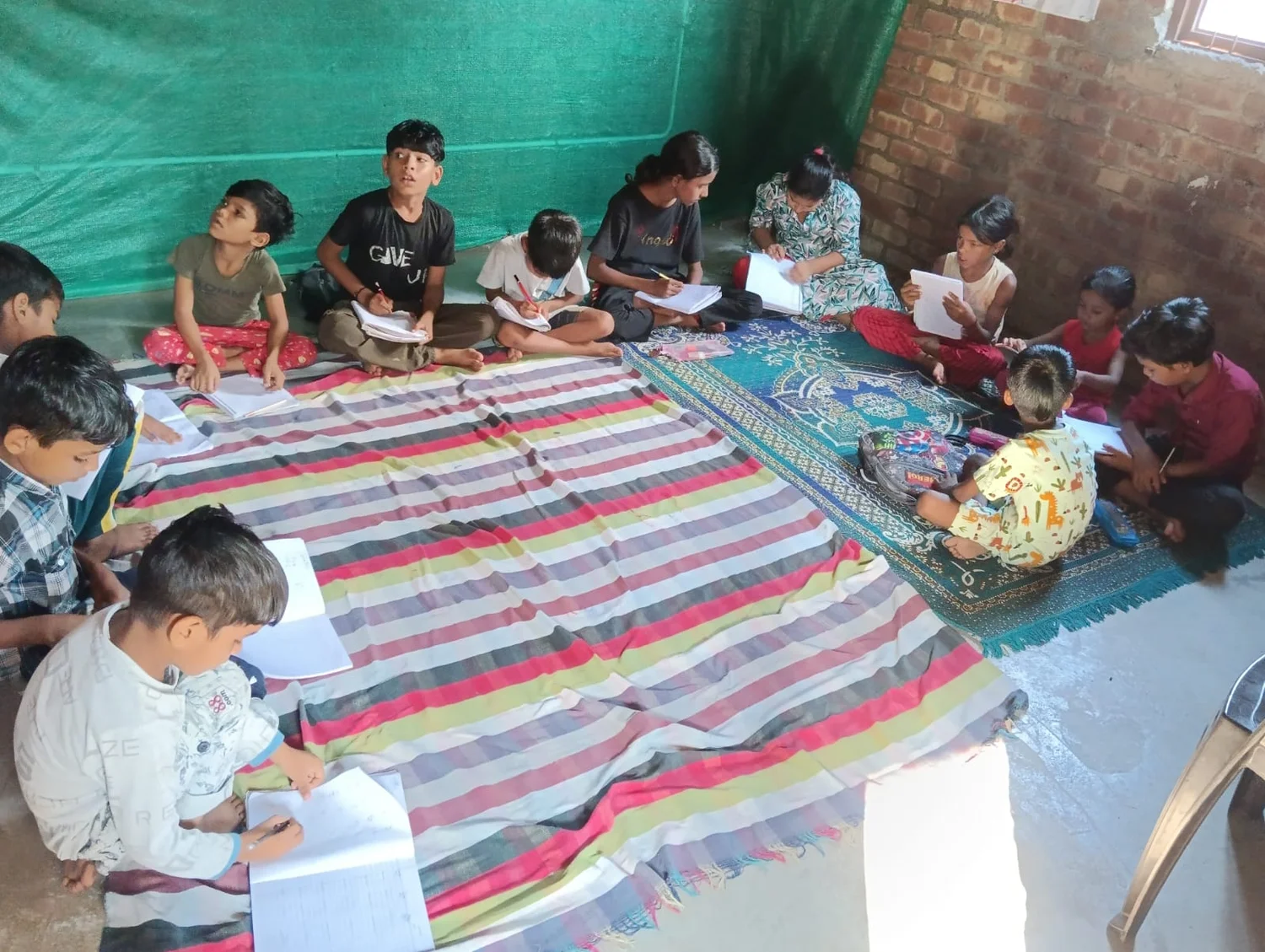 Learners read and write while seated around mats in the shared learning space.