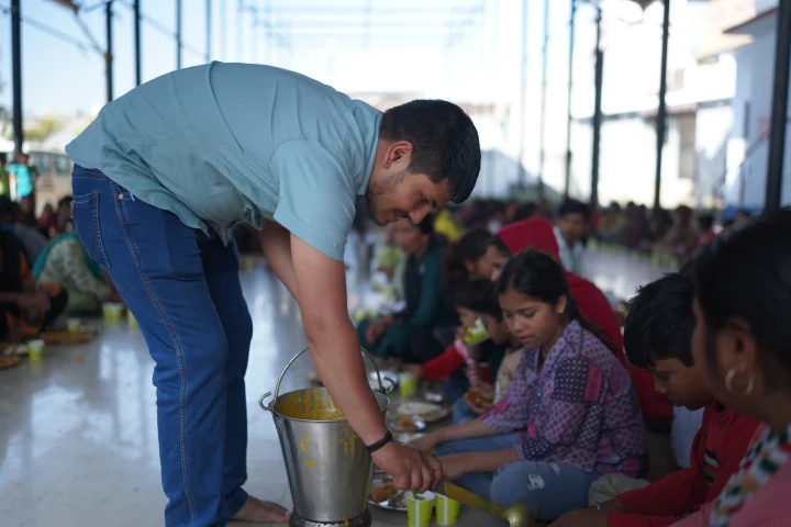 A volunteer serving children seated for lunch in a community hall