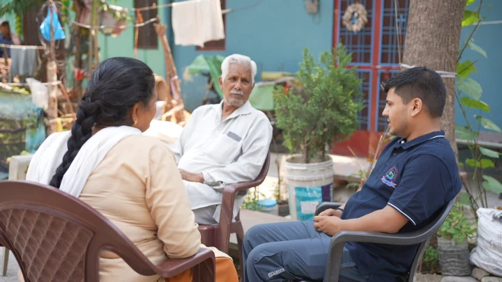 Dev Bhoomi Samiti team sitting with an older resident in a courtyard