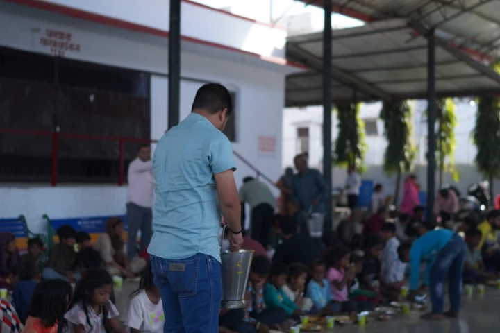 A volunteer carrying a serving bucket through a community dining hall