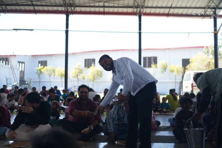 A volunteer serving meals to people seated in rows inside a community hall