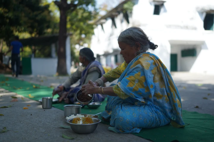 An older woman seated outdoors with a meal and drinking cup