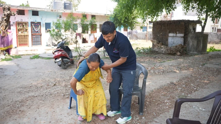 A volunteer assisting a seated older woman in a courtyard