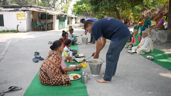 Dev Bhoomi Samiti volunteer serving food to residents seated in a community courtyard