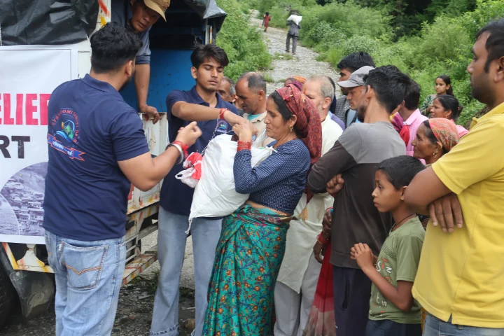 Dev Bhoomi Samiti volunteer distributing relief items to a group of residents