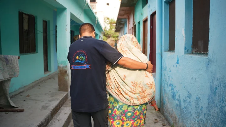 A volunteer walking beside an older woman in a residential lane