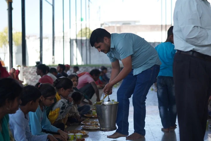 A volunteer serving a meal to children seated in a row