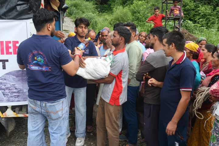 Volunteers handing a bag of relief supplies to residents beside a truck