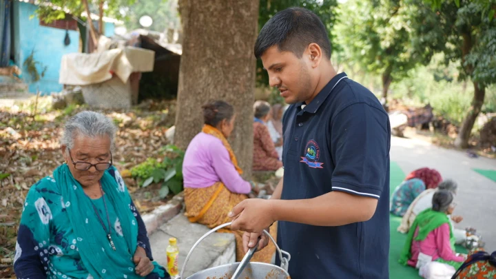 A volunteer serving food beside an older woman during a community meal