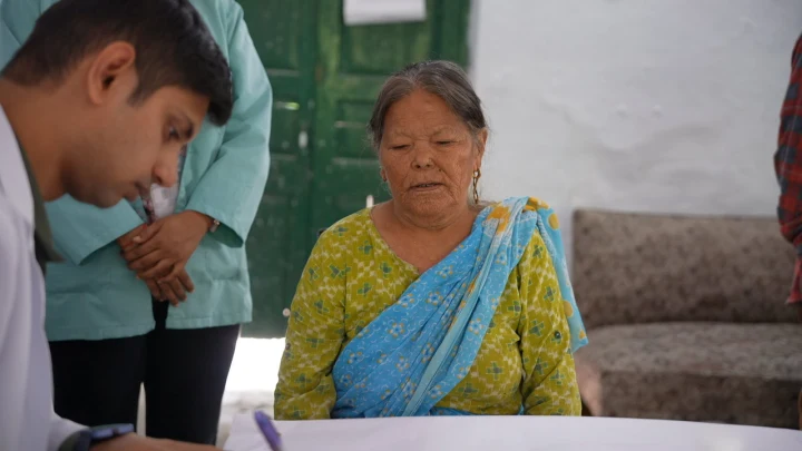 A volunteer speaking with an older woman seated outside her home